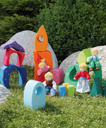 Pieces from the Grimm's fairytale village set loose on grass with waldorf dolls standing on top of the blocks