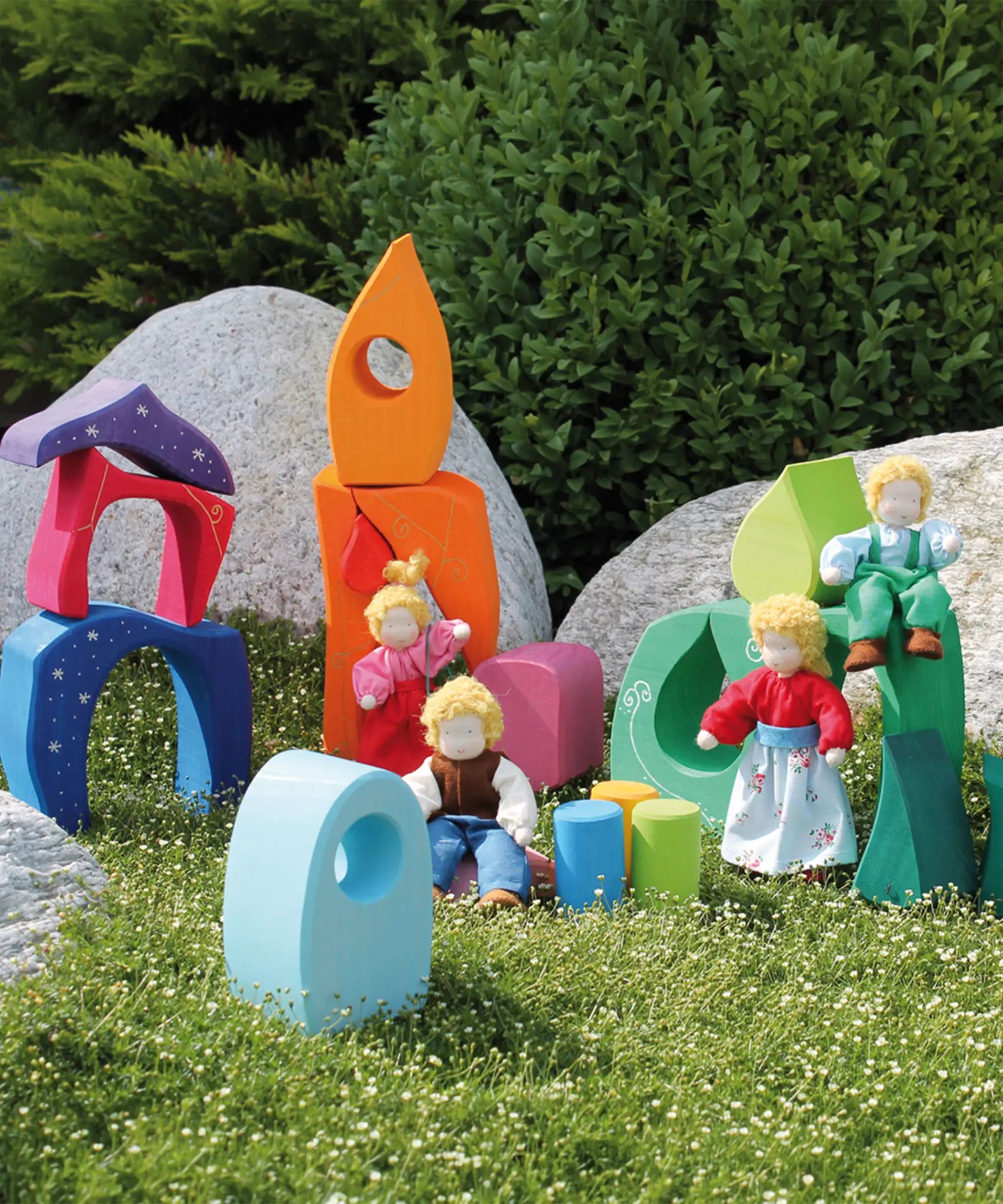 Pieces from the Grimm's fairytale village set loose on grass with waldorf dolls standing on top of the blocks