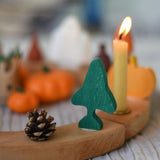 A Grimm's fir tree decorative figure placed on a natural wooden celebration ring. A lit candle and other Autumn themed decorations can be seen in the background. The decorative figures are part of a wide range of Waldorf inspired figures and celebration rings available here at Babipur. 