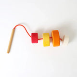 Grimms wooden threading needle with string fed through the bright and chunky disks 