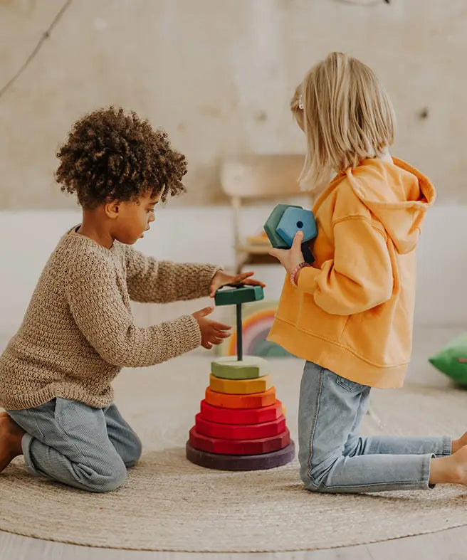 Children stacking wooden blocks from the Grimms Geometric stacking tower set in a playroom