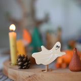 A Grimm's spooky ghost decorative figure placed on a natural celebration ring. A lit beeswax candle and other decorative figures can be seen in the background. The decorative figures are part of a wide range of Waldorf inspired figures and celebration rings available here at Babipur.