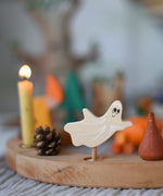A Grimm's spooky ghost decorative figure placed on a natural celebration ring. A lit beeswax candle and other decorative figures can be seen in the background. The decorative figures are part of a wide range of Waldorf inspired figures and celebration rings available here at Babipur.