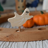 A close up of a Grimm's spooky ghost decorative figure placed on a natural celebration ring. A lit beeswax candle and other decorative figures can be seen in the background. The decorative figures are part of a wide range of Waldorf inspired figures and celebration rings available here at Babipur.