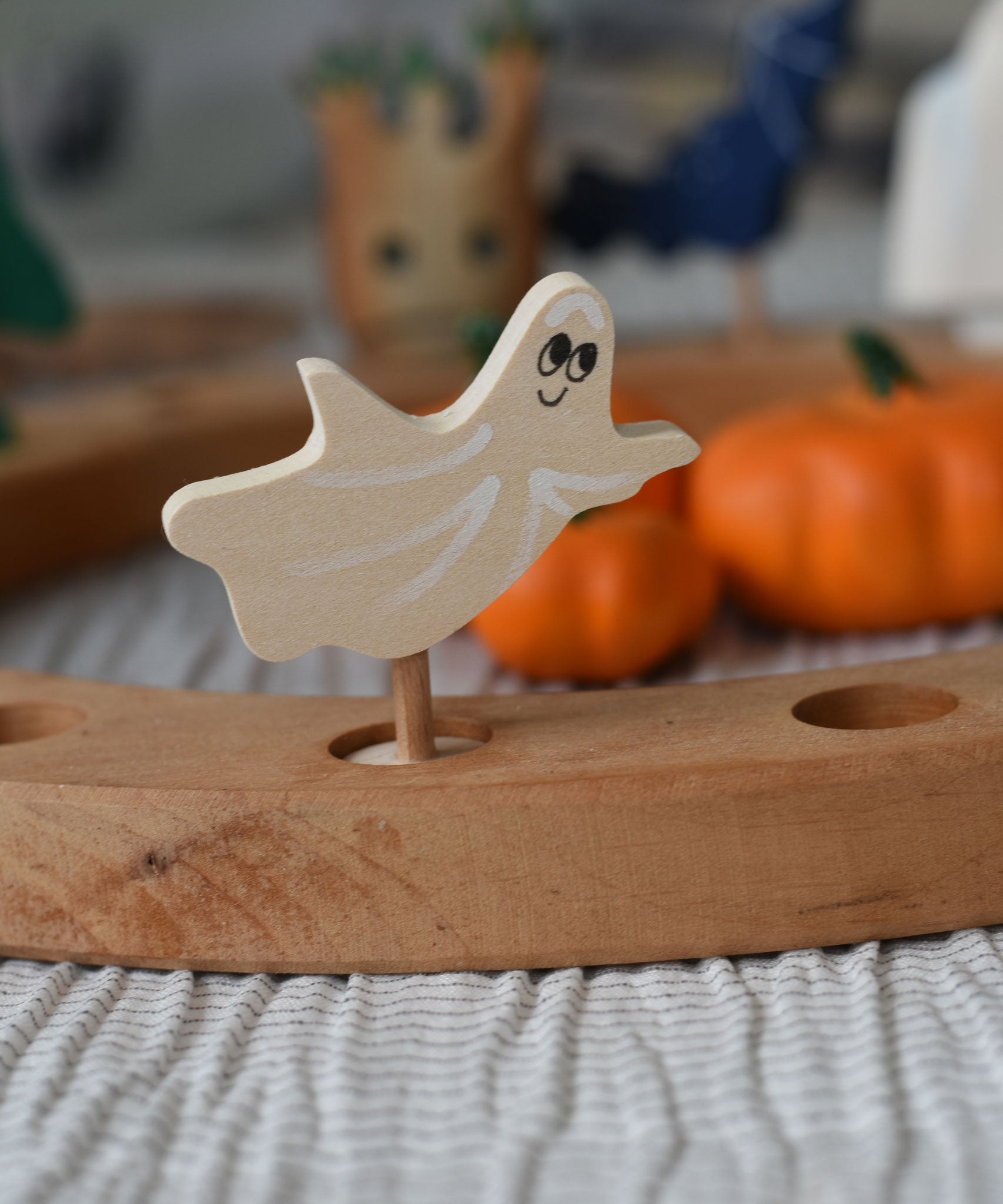 A close up of a Grimm's spooky ghost decorative figure placed on a natural celebration ring. A lit beeswax candle and other decorative figures can be seen in the background. The decorative figures are part of a wide range of Waldorf inspired figures and celebration rings available here at Babipur.