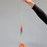 An adult holding each end of the giant Grimms spirelli available at Babipur. This  winding metal wire comes with coloured  wooden disks that make a noise when tipped over. 