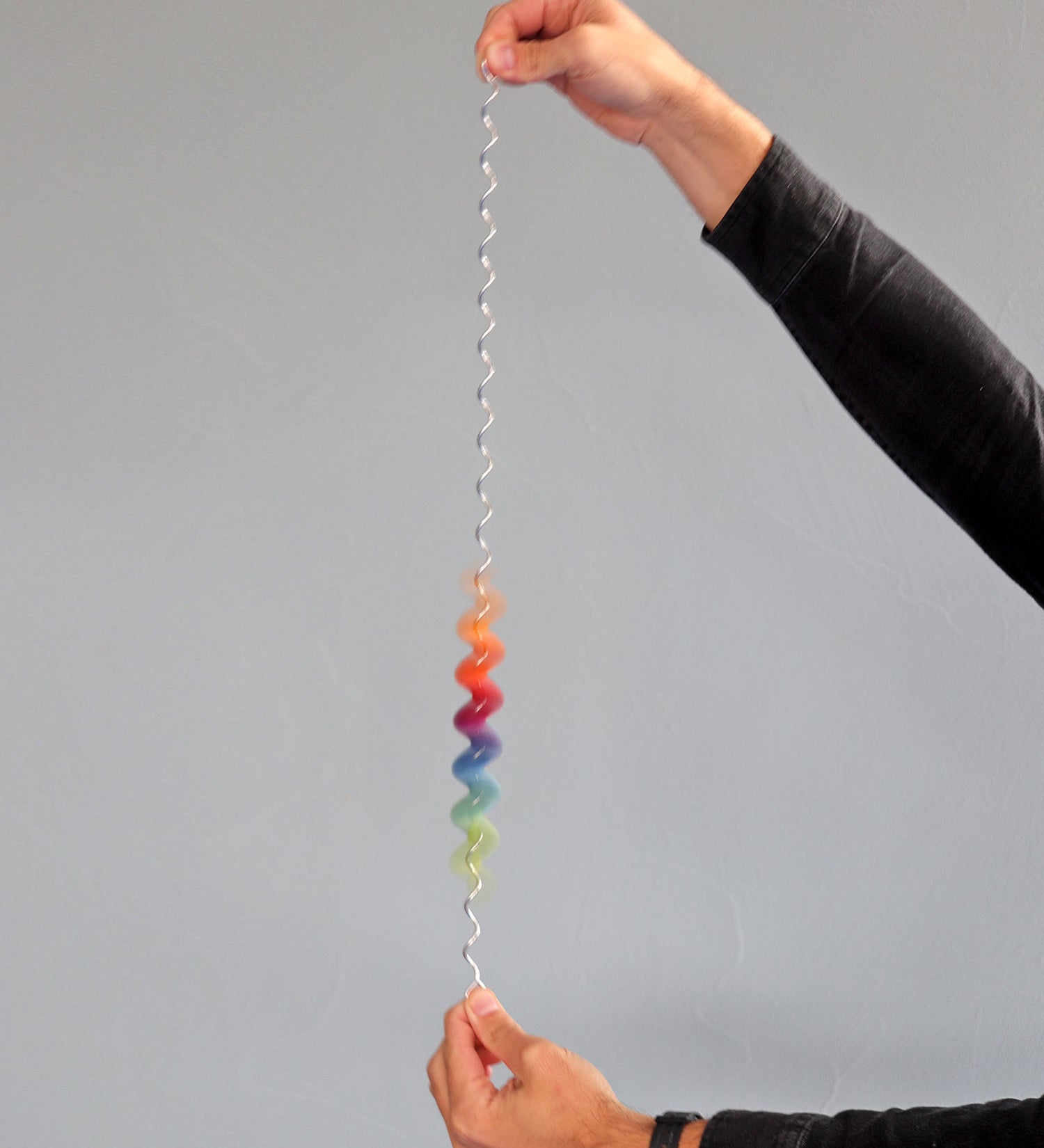 An adult holding each end of the giant Grimms spirelli available at Babipur. This  winding metal wire comes with coloured  wooden disks that make a noise when tipped over. 