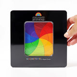 An adult hand holding a closed Grimms tin with a clear window in the front showing the Goethe magnetic puzzle set