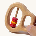 An adult's fingers holding the Grimm's Grasping Toy With 5 Rings.