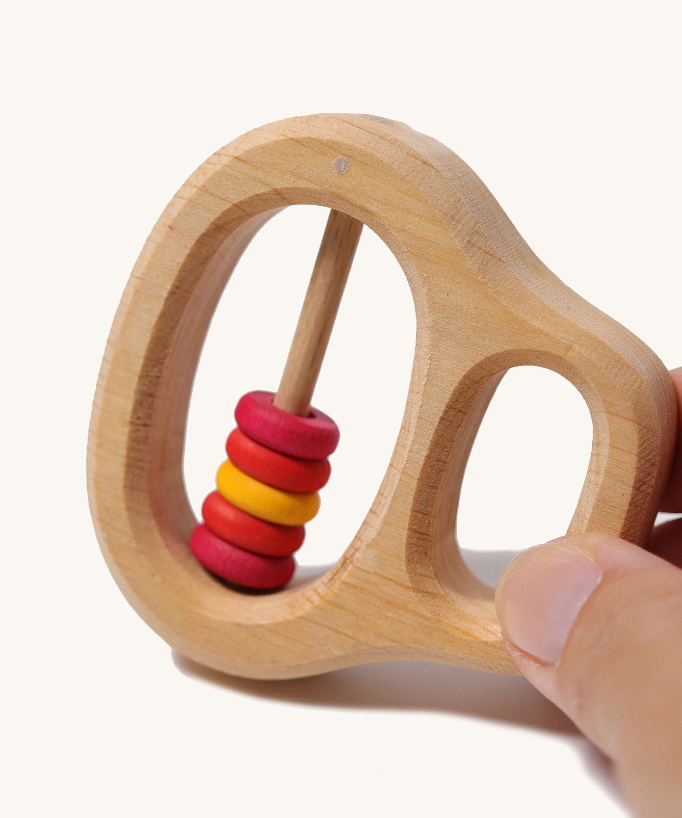 An adult's fingers holding the Grimm's Grasping Toy With 5 Rings.