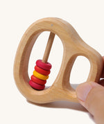 An adult's fingers holding the Grimm's Grasping Toy With 5 Rings.