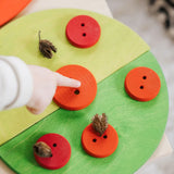 Child pointing at a wooden button piece on green Grimms semi circles