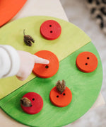 Child pointing at a wooden button piece on green Grimms semi circles