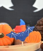 A close up of a Grimms bat decorative figure inserted in a Grimms wooden celebration ring with other Autumn decorative figures in the background available at Babipur.