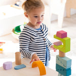 A child concentrating on building a beautiful wooden block stack using the Grimm's Cloud Play set