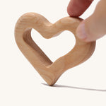 An adult's hand holding up the Grimm's Grasping Toy Smooth Heart.