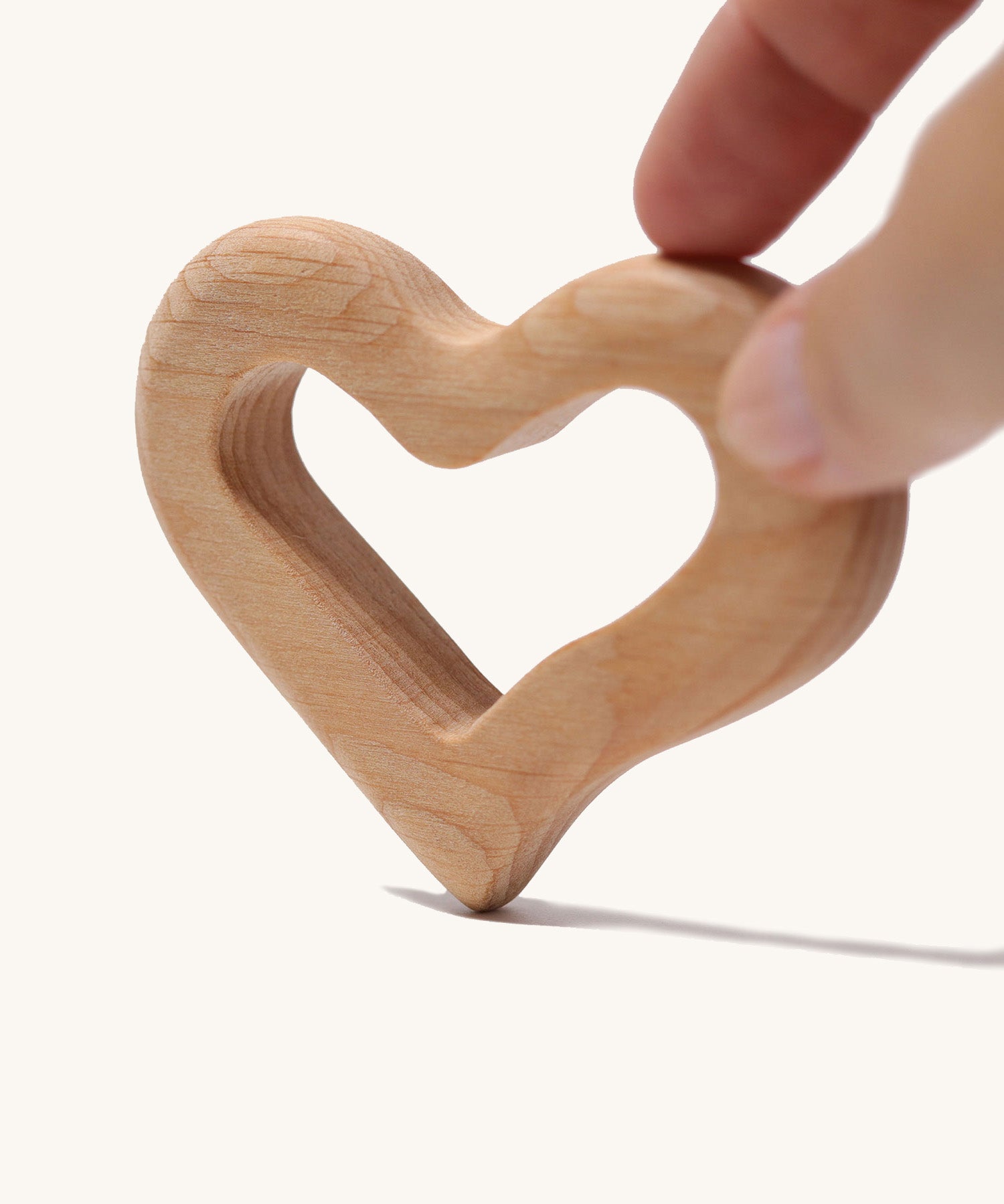 An adult's hand holding up the Grimm's Grasping Toy Smooth Heart.