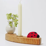 A single Grimms wooden celebration ring piece with a ladybird, white vase and candle 