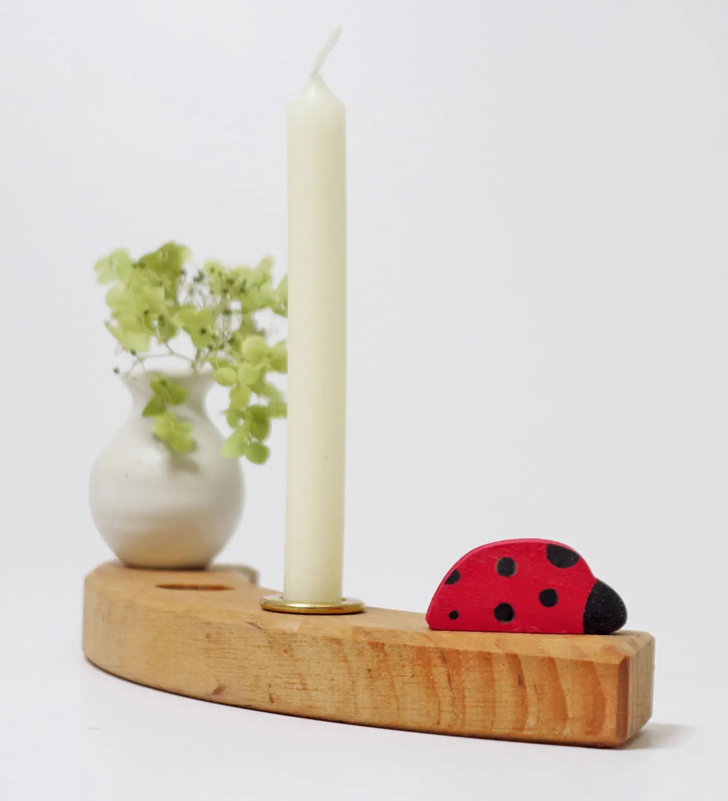 A single Grimms wooden celebration ring piece with a ladybird, white vase and candle 