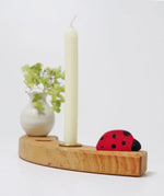 A single Grimms wooden celebration ring piece with a ladybird, white vase and candle 