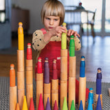 Child playing with the Grimm's large wooden building rollers placing friends peg dolls on the stacks.