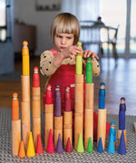 Child playing with the Grimm's large wooden building rollers placing friends peg dolls on the stacks.