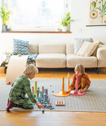 Children playing with Grimm's large building rollers pastel with other wooden toys.