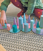 Child playing with Grimm's large building rollers in pastel , semi circles and forest pieces.