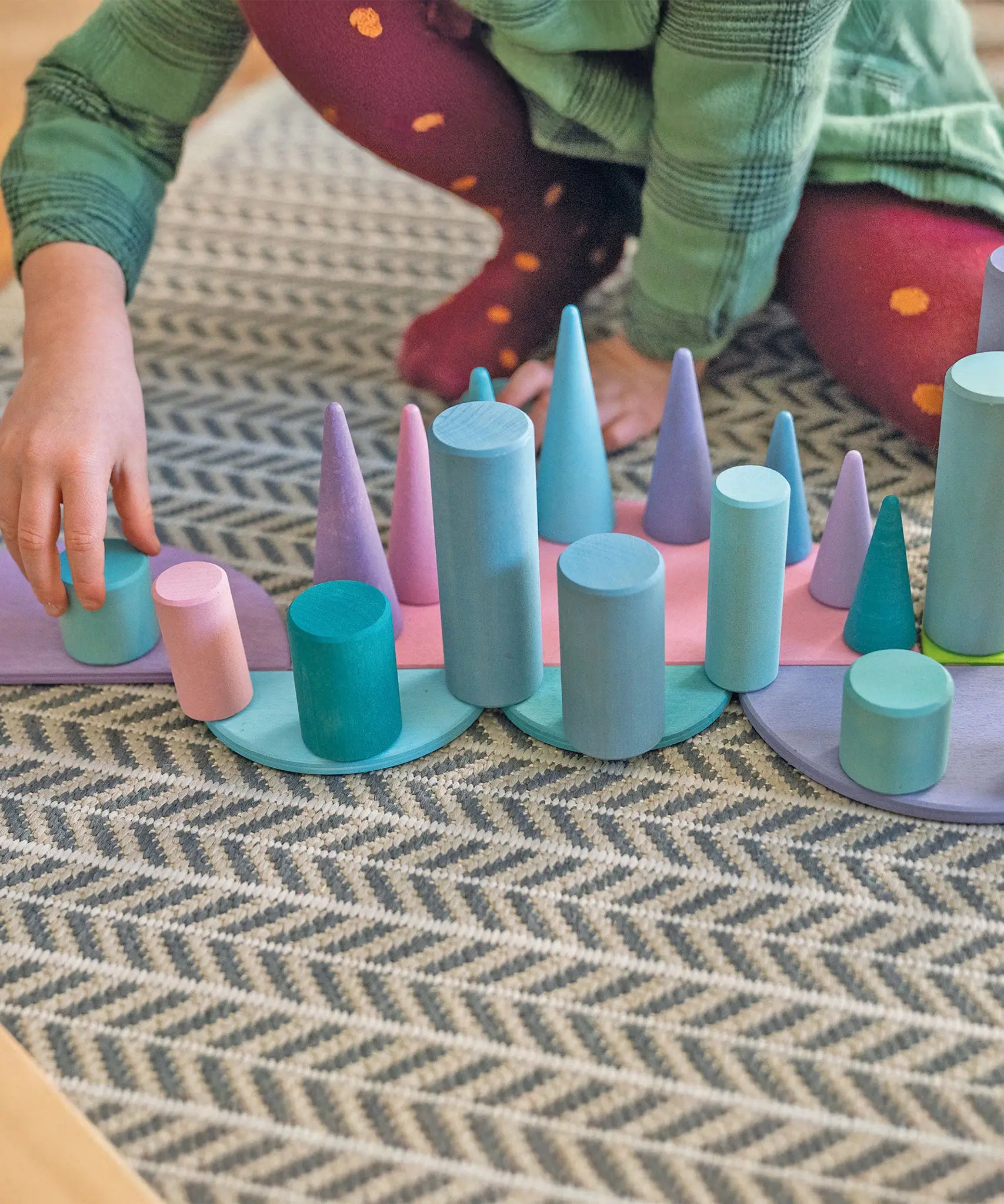 Child playing with Grimm's large building rollers in pastel , semi circles and forest pieces.