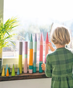 Child stacking Grimm's large building rollers pastel with forest pieces.