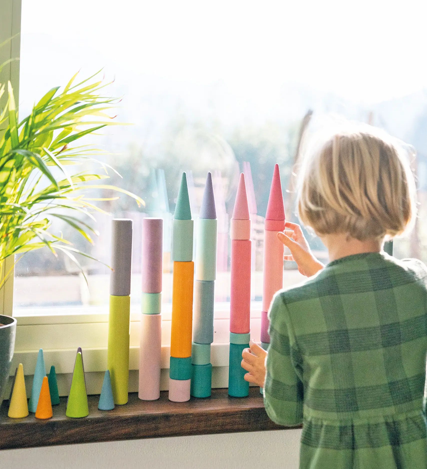 Child stacking Grimm's large building rollers pastel with forest pieces.
