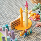 Child playing with Grimm's wooden open ended toys including large building rollers in pastel, friends peg dolls, forest pieces and cars.