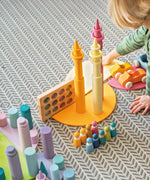 Child playing with Grimm's wooden open ended toys including large building rollers in pastel, friends peg dolls, forest pieces and cars.