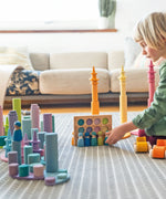 Child playing with Grimm's wooden open ended toys including large building rollers in pastel, friends peg dolls, forest pieces and cars.