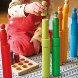 Child playing with the Grimm's large building rollers in bright rainbow colours stacking friends peg dolls on top. 