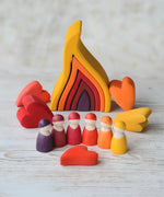 Grimms handcrafted wooden large fire set in a display with heart shaped pieces and peg dolls in matching warm colours