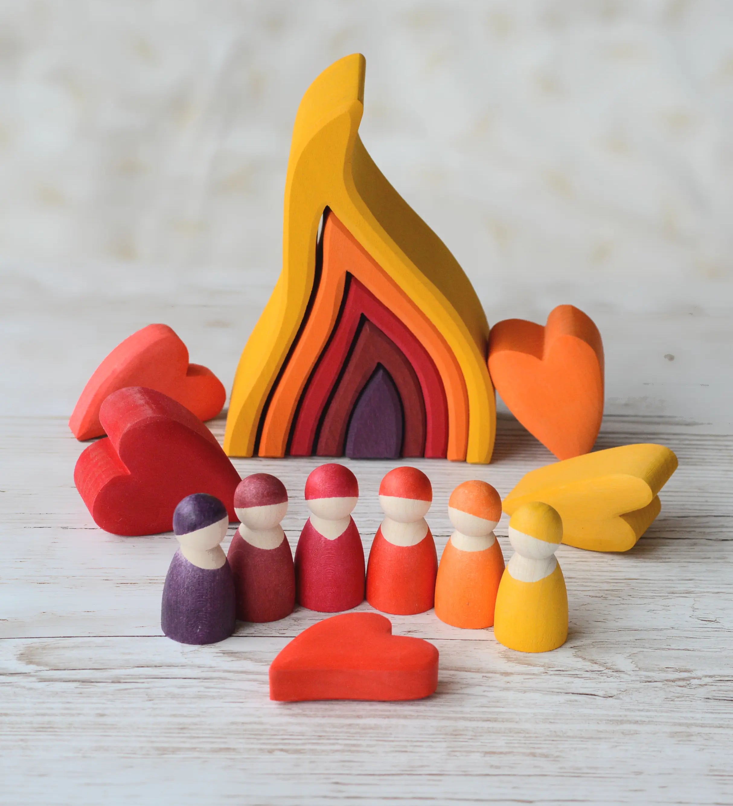 Grimms handcrafted wooden large fire set in a display with heart shaped pieces and peg dolls in matching warm colours