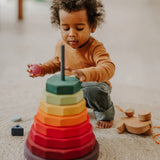 Grimms large wooden geometric stacking set standing near a child playing with loose blocks