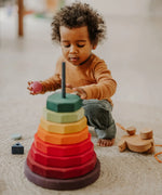 Grimms large wooden geometric stacking set standing near a child playing with loose blocks