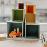 Grimms wooden large pastel boxes stacked on top of eachother with a orange car hiding inside one box
