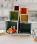 Grimms wooden large pastel boxes stacked on top of eachother with a orange car hiding inside one box
