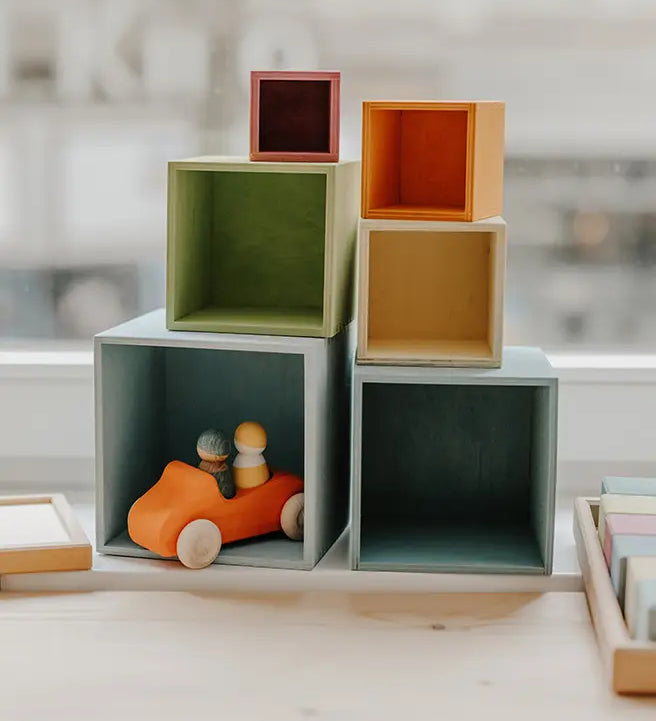 Grimms wooden large pastel boxes stacked on top of eachother with a orange car hiding inside one box