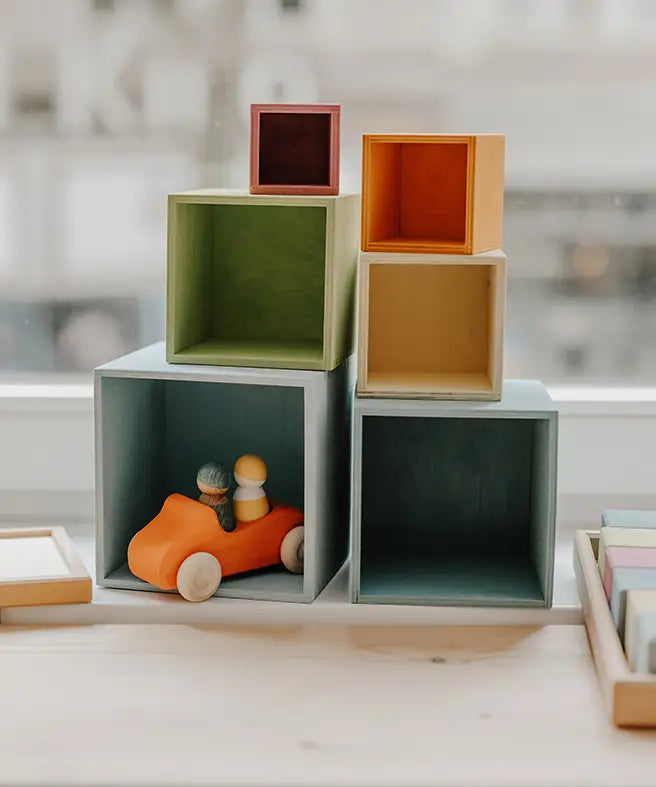 Grimms wooden large pastel boxes stacked on top of eachother with a orange car hiding inside one box