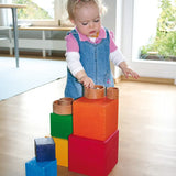 Child playing with the Grimm's Large rainbow building boxes set on a wooden floor with other loose parts
