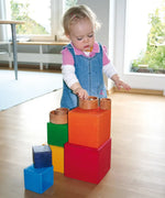 Child playing with the Grimm's Large rainbow building boxes set on a wooden floor with other loose parts