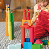 Child playing with the Grimm's large building rollers in bright rainbow colours with wooden blocks and friends peg dolls.
