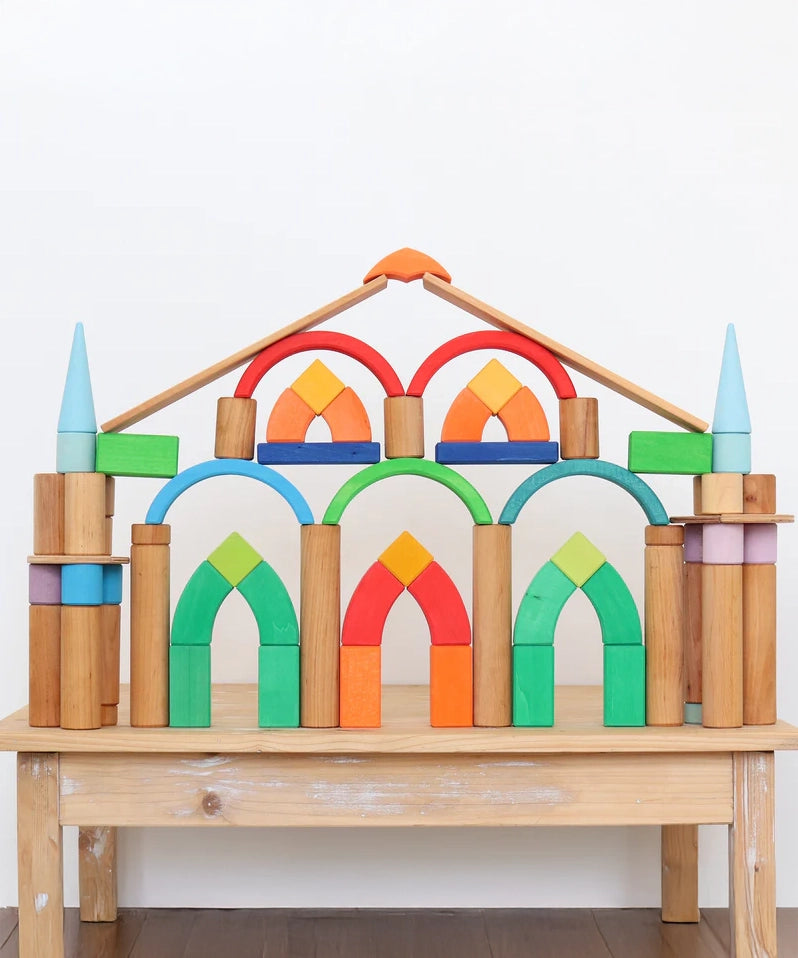 Grimm's Romanesque building blocks and natural rollers used to create a structure on a wooden table. 