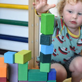 Grimm's large stepped pyramid coloured wooden block set played with in the Babipur playroom. Close up of child's hand reaching for a green block.
