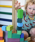Grimm's large stepped pyramid coloured wooden block set played with in the Babipur playroom. Close up of child's hand reaching for a green block.
