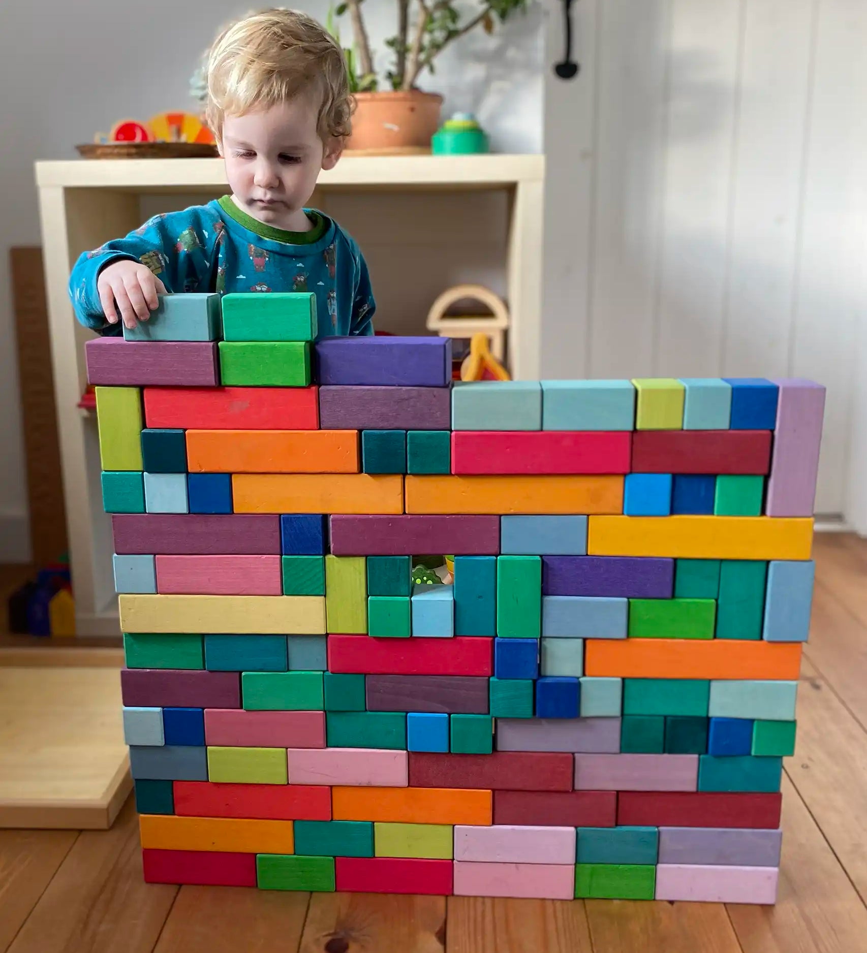 Grimm's large stepped pyramid coloured wooden block set used to create a large wall like structure by a child.